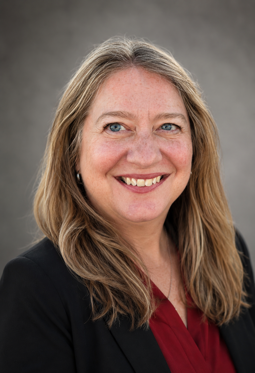 woman with long hair blue eyes smiling wearing red shirt and black blazer